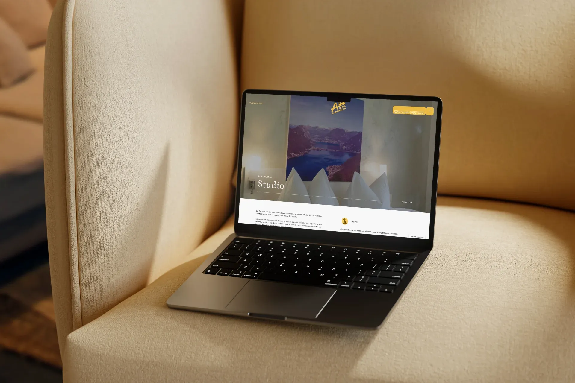 Hotel Acquarello, mockup laptop su poltrona beige con pagina camera Studio e foto panoramica